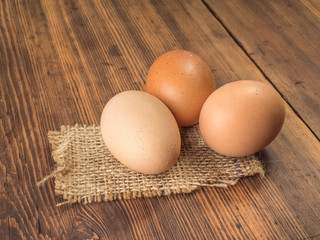 Brown chicken eggs lay on a piece of burlap on a wooden table from the old boards. Three fresh chicken eggs close-up, background for advertising or Easter greetings, rustic style