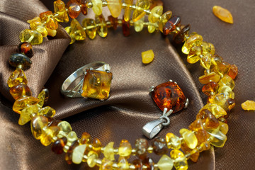 closeup jewerly with  authentic  natural baltic amber : bracelet, silver ring and pendant, on brown atlas surface. soft focus, shallow DOF.