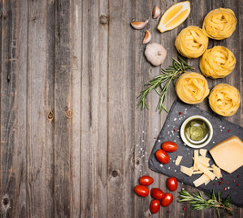 Fettuccine background frame with ingredients for cooking pasta on weathered wood, top view.