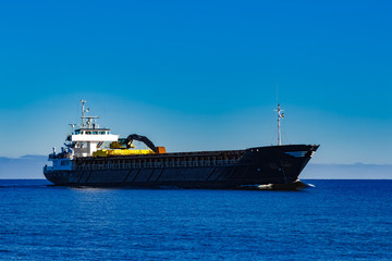 Fototapeta premium Black cargo ship with long reach excavator moving by baltic sea
