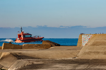 Red pilot ship moving at speed past the breakwater dam