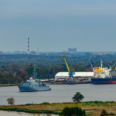 Fototapeta premium Military ship sailing past the cargo port in Riga, Latvia
