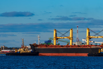 Black cargo ship mooring at the port with tug ship support