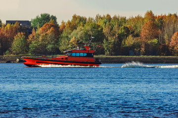 Fototapeta premium Red pilot ship moving past the autumn trees in Europe