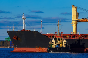 Black cargo ship mooring at the port with tug ship support