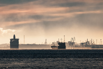 Fototapeta premium Cargo ship silhouette entering a port of Riga at the morning