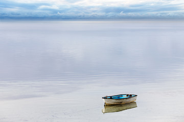A small wooden dinghy moored on a calm bay of water as a storm passes by on the horizon.