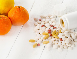 Citrus fruits and different pills on a white wooden background.