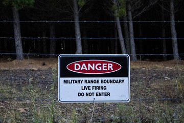 Fototapeta premium Danger Military range boundary sign on barbed wire fence in front of forest