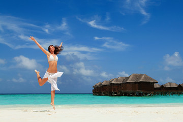 Happy young woman jumping on the beach. Happy lifestyle. White sand, blue sky and crystal sea of tropical beach. Vacation at Paradise. Ocean beach relax, travel to islands