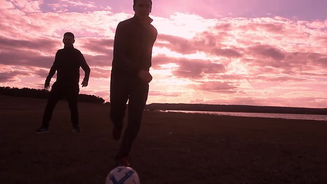 Beautiful sunset and silhouettes of men playing football, kick a soccer ball, goalkeeper catches ball. Silhouette of soccer player ready to execute penalty kick on the field.