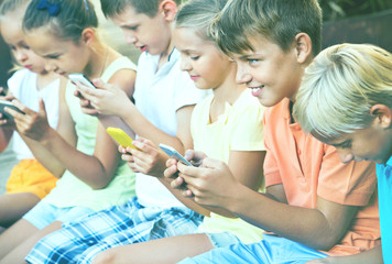 Obraz na płótnie Canvas Busy children holding smartphones and sitting