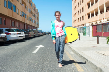 Sporty lifestyle. Young teenage girl with surfboard walking on street.