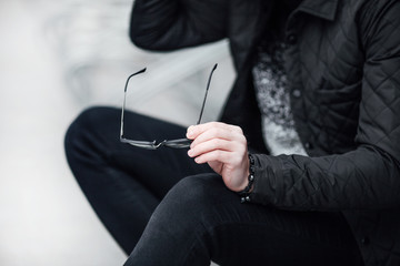 Fashionable man sitting near the wall with glasses on hands