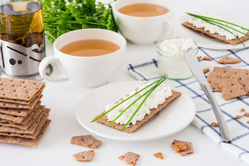 Snack with fresh tea and rye crispy bread (Swedish crackers) with cottage cheese, decorated with thin green onion, on white background. Healthy food concept for breakfast