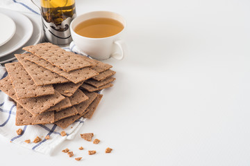 Brown rye crispy bread (Swedish crackers) on piece of cloth with plates, cup filled with herbal tea...