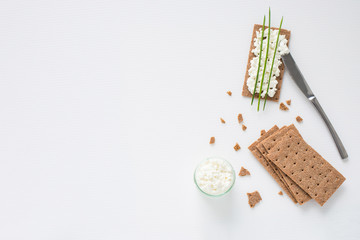 Brown rye crispy bread (Swedish crackers) with spread cottage cheese, decorated with thin green onion, on white background with space for text, top view. Healthy snack concept
