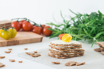Rye crispy bread (Swedish crackers) stacked in the form of cake in layers with soft cheese, cherry tomatoes and rosemary on white background. Healthy snack concept