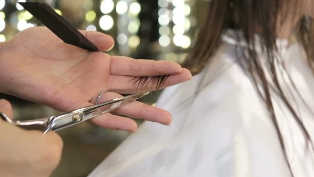 Close-up of a barber cuts hair strands. Work in the salon. Barber cuts hair with scissors. Barber cuts woman's hair, hairdresser makes haircut. Woman comes to beauty salon, fashion and style for women