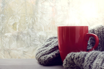 Obraz na płótnie Canvas warming cozy atmosphere/ red mug of hot drink with a fluffy blanket on the background of frozen window
