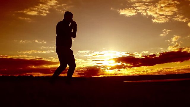 Silhouette of man boxing with shadow on the beatch at sunset intentional sun flare and vintage color. Man Engaged In Melee Combat Sports Boxing At Sport Sunset Shadow Boxing