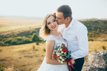 Gorgeous bride, groom kissing and hugging near the cliffs with stunning views
