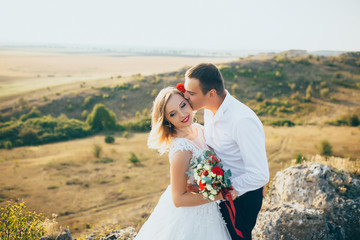 Fototapeta na wymiar Gorgeous bride, groom kissing and hugging near the cliffs with stunning views