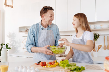 Overjoyed smiling father and daughter cooking salad together
