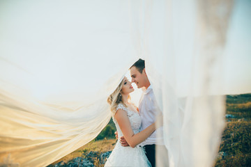 wedding couple covered with bridal vail at sunset - obrazy, fototapety, plakaty