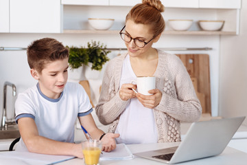 Pleasant little boy doing home assignment with his mother