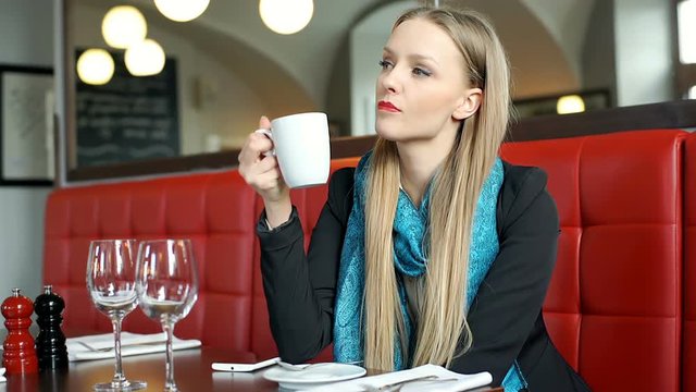Elegant woman drinking coffee in posh restaurant and doing serious look to the camera
