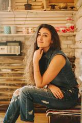 curly hipster girl in tattered jeans on a wooden background.