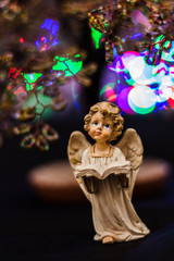 Figure of an angel reading a book against a tree and multicolored lights/  Figure of an angel reading a book against a tree and multicolored lights
