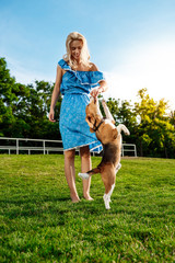 Young beautiful blonde girl walking, playing with beagle dog in park.