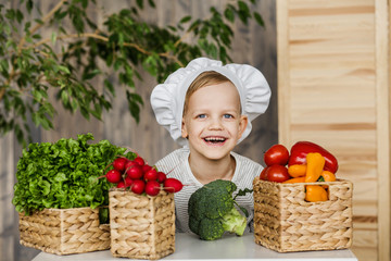 Handsome little kid in chef uniform with vegetables. Cooking in kitchen at home. Vegetarian. Healthy food