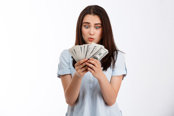 Young beautiful surprised brunette business girl holding money over white background
