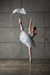Ballerina in white costume dancing with white cloth in studio with grey wall