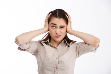 Young beautiful confused crazy brunette businessgirl clutching her head looking up over white background