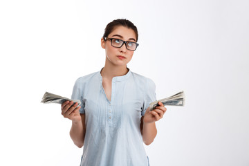 Obraz premium Young confident beautiful business girl in glasses holding money dreamy looking up over white background 