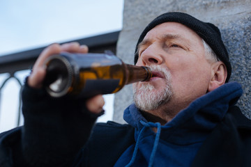 Portrait of sad man keeping glass bottle near mouth