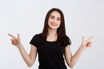 Young beautiful smiling girl in black t-shirt pointing fingers in opposite sides over white background