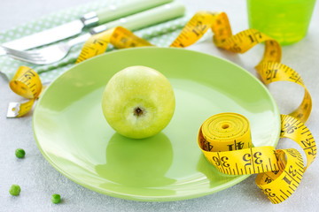 Green apple on green plate with measuring tape on white background