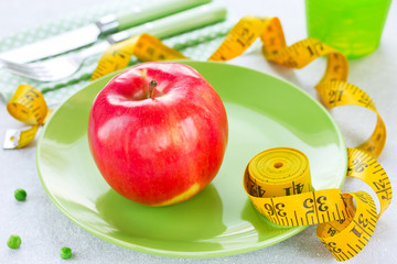 Big ripe apple on green plate with measuring tape on white background