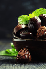 Chocolate candies, assorted, decorated with mint leaves, dark background, low key, selective focus
