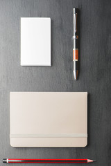 Business card, pen, pencil and notebook on black background. Vertical shoot.