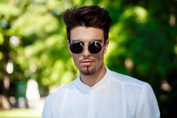 Young successful businessman in sunglasses walking around sunny city.