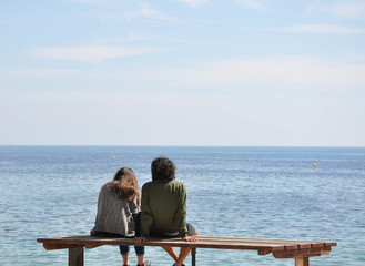 Young couple of people sitting on a bench and looking at the sea