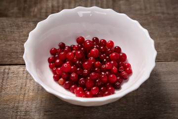 Unfrozen cranberry in the white bowl on the old wooden table. Healthy food, vitamins. Rustic background. Healthy eating, dieting.