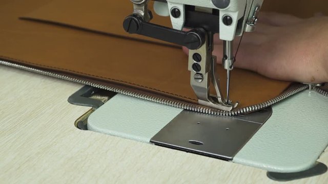 Closeup view of man's hand stitching leather product with modern sewing machine. Making a leather handbag. 
