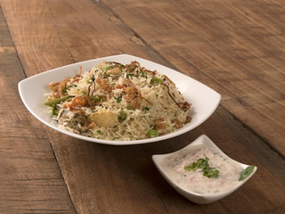 Veg pulav served in a white bowl with raita(curd) on wooden background